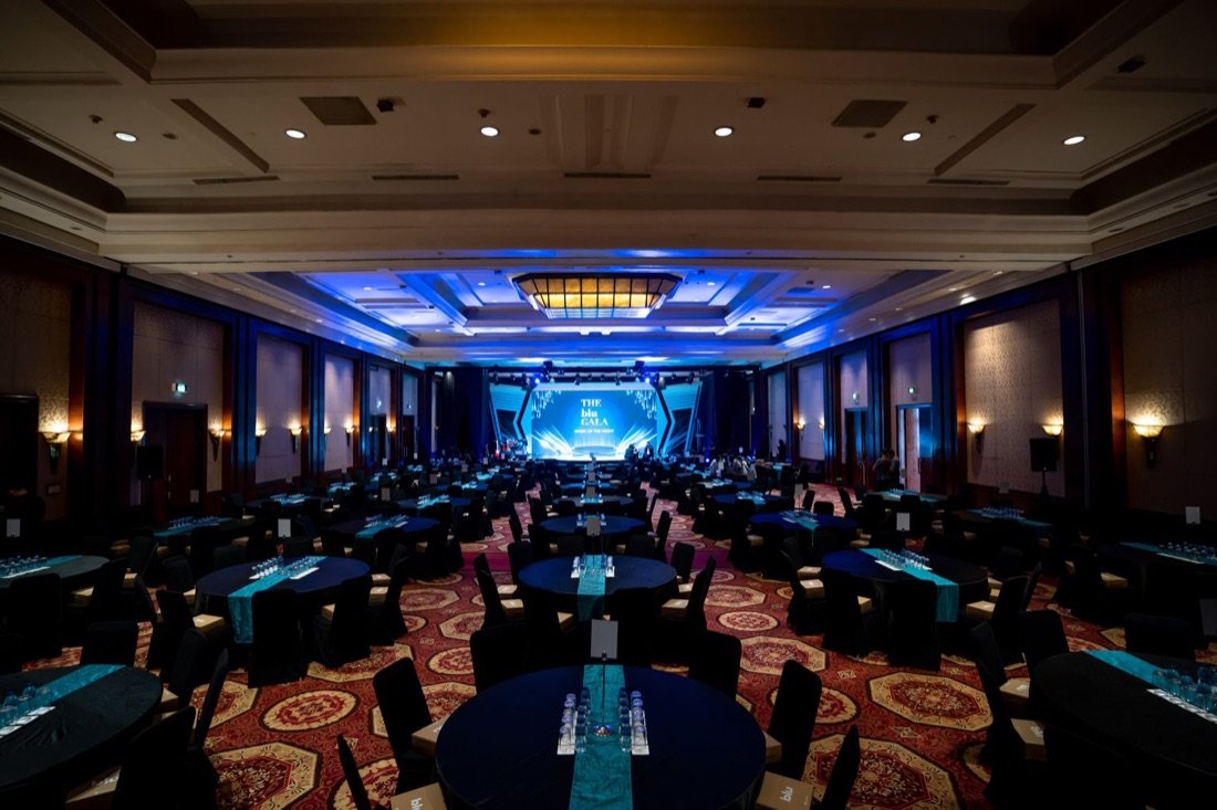 Ballroom megah The Blu Gala dengan meja banquet tertata dan panggung menyala