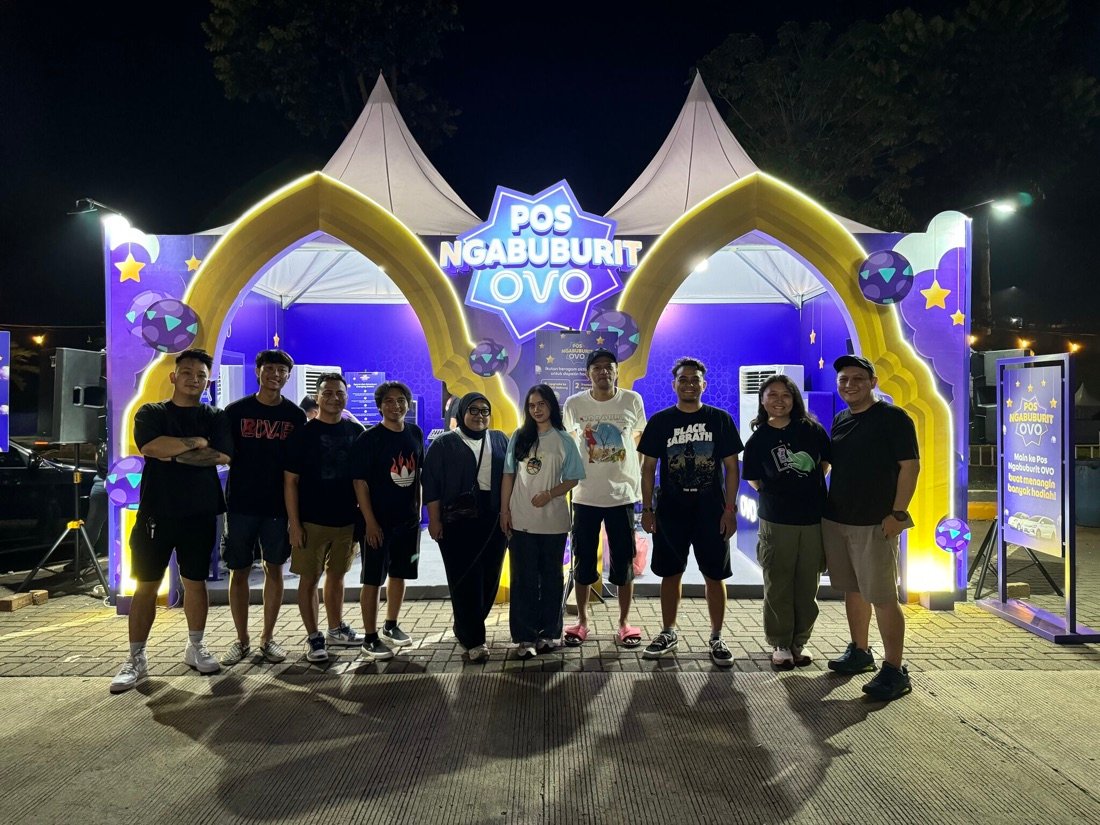 Instalasi arch Pos Ngabuburit OVO menyala dan tim aktivasi berpose di malam hari